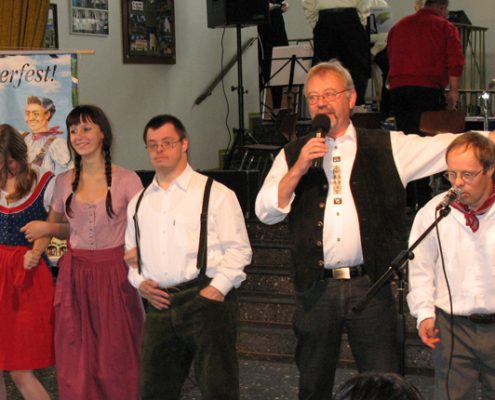 Eine Frau und ein Mann stehen auf einer Bühne. Der Mann hält ein Mikrofon und spricht. Es sieht aus wie ein Fest.