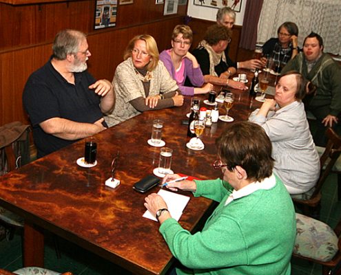 Eine Gruppe von Menschen sitzt an einem Tisch in einer Bar. Sie unterhalten sich und trinken etwas.