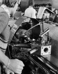 Ein Mechaniker arbeitet an einer komplexen Maschine in einer Werkstatt, um Reparaturen und Wartungsarbeiten durchzuführen. Die Umgebung zeigt verschiedene Werkzeuge und Teile, die für technische Arbeiten benötigt werden.