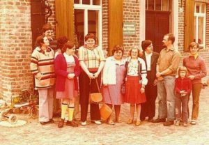 Eine Familie steht vor einem Haus. Es sind Erwachsene und Kinder. Alle lächeln.
