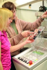 Mädchen mit blonden Haaren und Erwachsene, die gemeinsam über eine Broschüre diskutieren, während sie an einem Tisch sitzen.