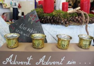 Adventskranz mit goldenen Kerzenhaltern und roten Kerzen auf einem festlich dekorierten Tisch, umgeben von Tannenzweigen und Weihnachtsdekoration. Ideal für die Adventszeit und festliche Anlässe.