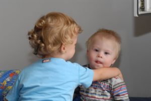 Zwei Kinder umarmen sich. Eines hat ein blaues T-Shirt an.