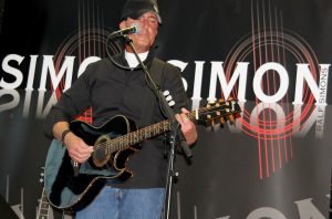 Musiker mit Gitarre auf der Bühne, vor einem Banner mit dem Schriftzug "Montisimo", während eines Live-Auftritts.