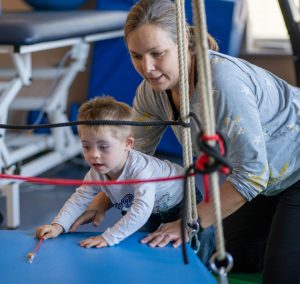Eine Mutter hilft ihrem kleinen Kind beim Spielen auf einer Sportmatte in einem Fitnessstudio.