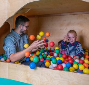 Ein Mann und ein Kind spielen in einem Ballbad. Es sind viele bunte Bälle.