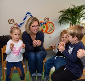 Kinder essen Kekse. Ein Mann sitzt und lacht.