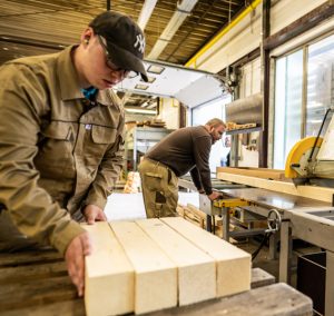 Holzstücke liegen auf dem Tisch. Ein Mann arbeitet mit Werkzeugen.