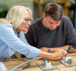 Zwei Personen arbeiten an Elektroteilen. Eine Person hilft der anderen.