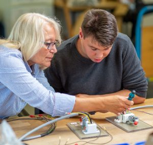 Zwei Personen arbeiten an einer Technik-Aufgabe. Eine Person hält etwas fest, die andere schraubt.