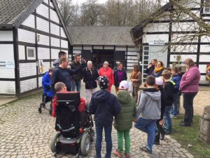 Gruppe von Menschen bei einer Führung in einem historischen Freilichtmuseum mit traditionellen Fachwerkhäusern.