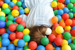 Ein Kind liegt in einem Ballbad voller bunter Bälle.