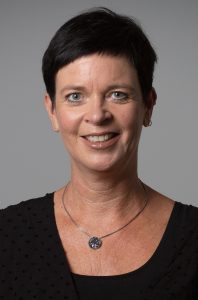 Eine Frau lächelt in die Kamera. Sie hat kurze, dunkle Haare und trägt eine Kette.