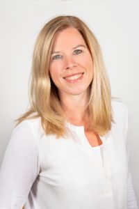 Eine Frau lächelt in die Kamera. Sie trägt ein weißes Oberteil.