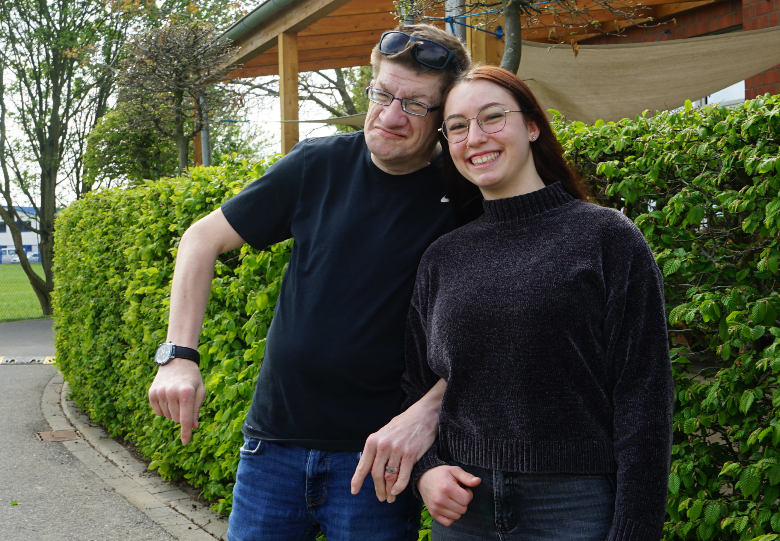 Ein Mann und eine Frau stehen nebeneinander. Der Mann trägt ein schwarzes T-Shirt, die Frau einen Pullover. Beide lächeln.