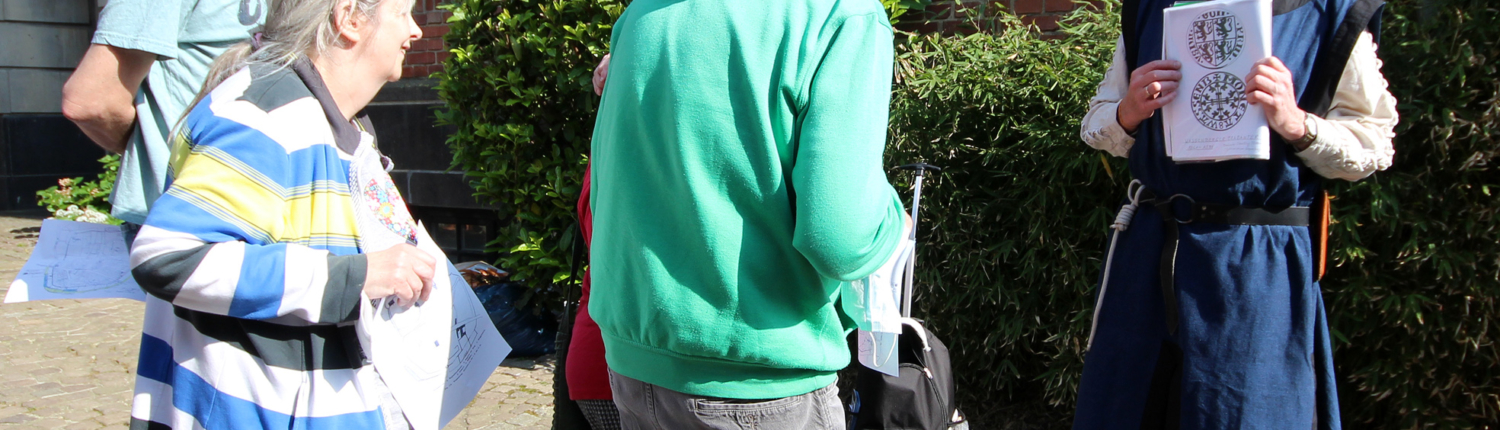 Eine Gruppe Menschen steht vor einem Haus. Eine Person trägt mittelalterliche Kleidung.