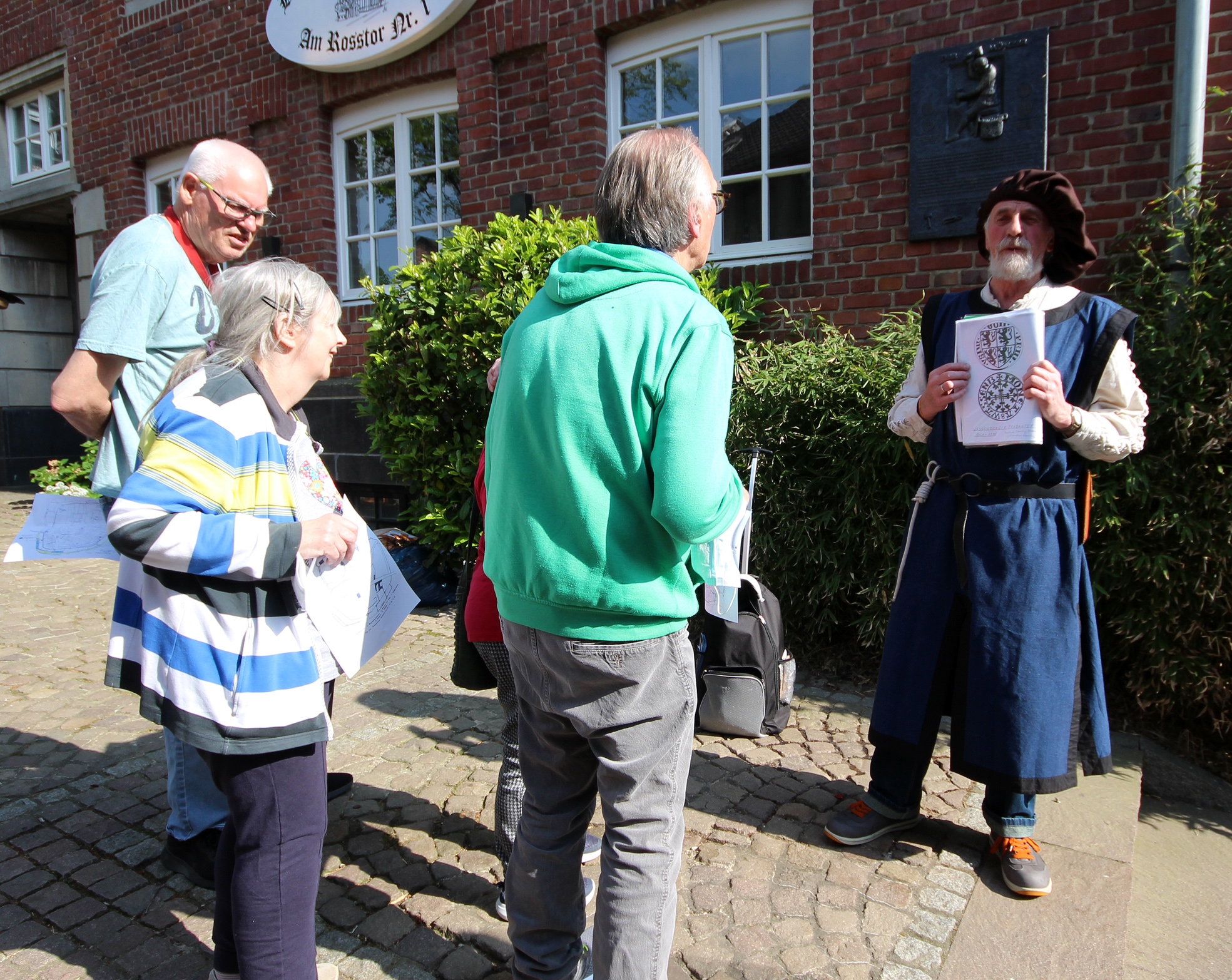 Eine Gruppe Menschen steht vor einem Haus. Eine Person trägt mittelalterliche Kleidung.