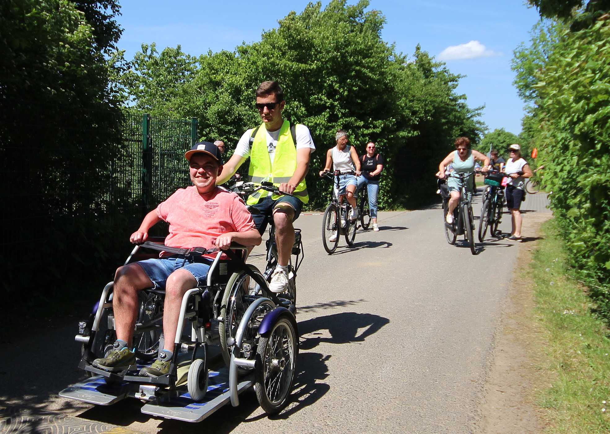 Menschen fahren mit Fahrrädern und Rollstühlen auf einem Weg.