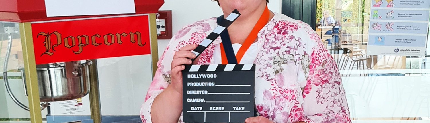 Frau mit Klappe und buntem Outfit steht vor einem Popcornstand auf einer Veranstaltung.