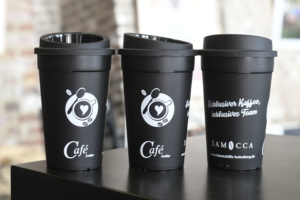 Drei schwarze Kaffeebecher mit Logo auf einem Tisch, ideal für einen modernen Café-Look.