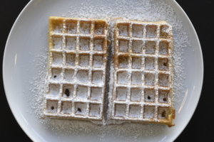 Waffeln auf einem Teller. Die Waffeln sind mit Puderzucker bedeckt.