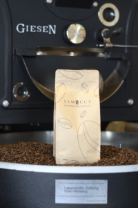 Block von geröstetem Kaffee vor einer Kaffeeröstmaschine, umgeben von Kaffeebohnen. Ideal für Kaffeeliebhaber und Röstereien.