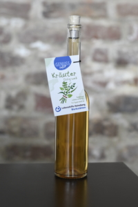 Flasche mit hochwertigem Olivenöl, etikettiert mit einem grünen Kräuter-Motiv, vor einer Backsteinmauer platziert. Ideal für mediterrane Gerichte und Salate.