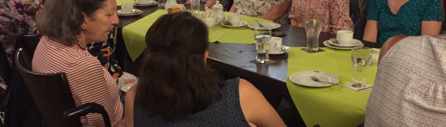 Gruppenfoto von Menschen, die an einem gedeckten Tisch in einem Restaurant sitzen. Die Teilnehmer sind in geselliger Runde versammelt und genießen ein gemeinsames Essen.