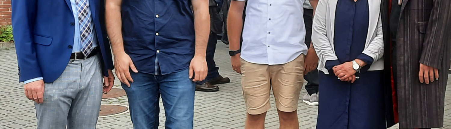 Gruppenfoto von fünf Personen vor einem modernen Gebäude, die in informeller Kleidung lächeln und sich für die Kamera aufstellen.