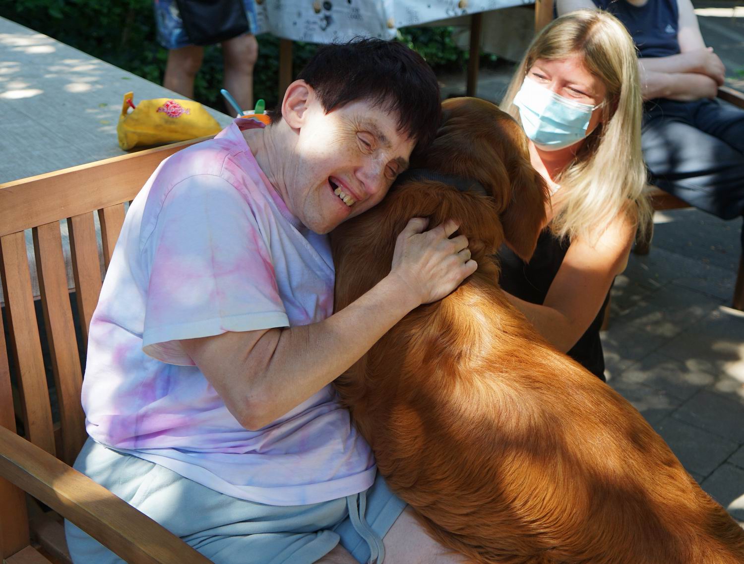 Ein Mann umarmt einen Hund. Der Hund ist rotbraun. Beide lächeln.