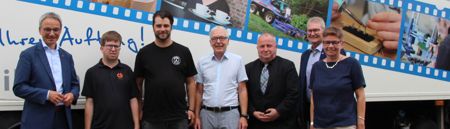 Gruppenfoto von Mitarbeitern des Werkstatt für behinderte Menschen vor einem Fahrzeug, das mit Informationen und Bildern zur Einrichtung gestaltet ist.