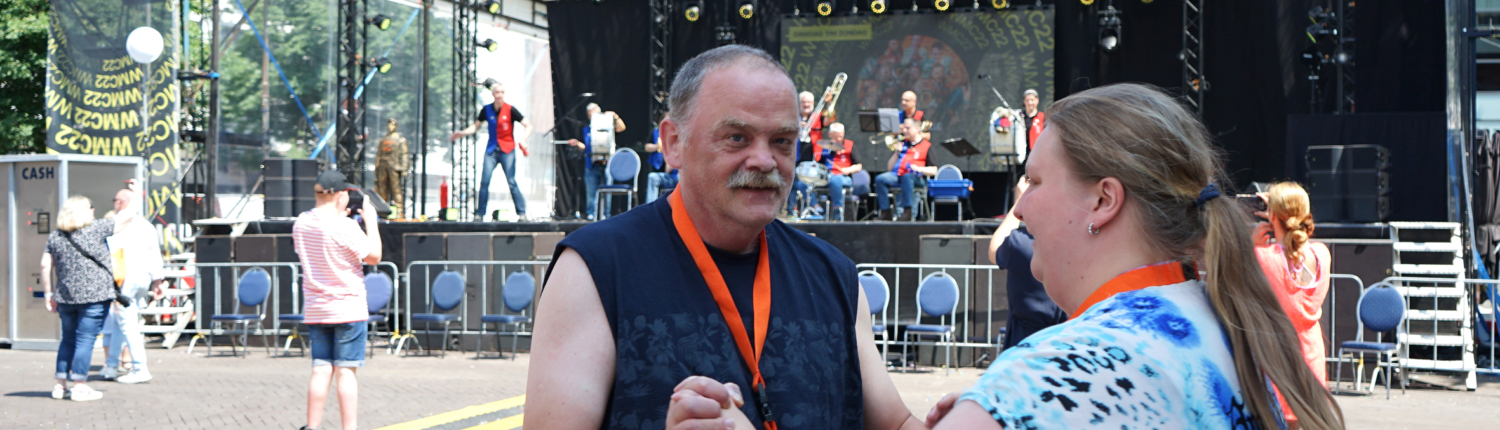 Zwei Personen tanzen und feiern auf einem Festivalgelände vor einer Bühne, umgeben von anderen Besuchern.