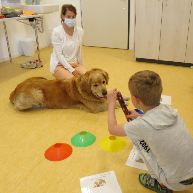 Ein Junge und ein Mädchen sitzen mit einem Hund im Raum. Der Hund liegt auf dem Boden.