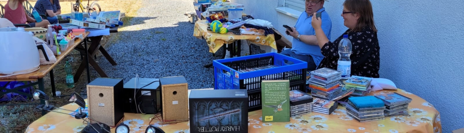 Ein Stand mit vielen Büchern, CDs und Dingen zum Kaufen. Zwei Männer schauen sich etwas an.