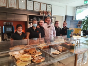 Mitarbeiter eines Bäckereibetriebs stehen hinter einer Theke mit frischen Backwaren, darunter Brot und Gebäck, in einem einladenden Verkaufsraum.