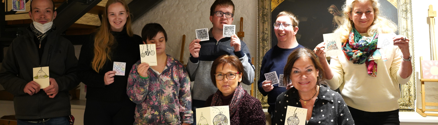 Gruppe von sieben Personen, die in einem gemütlichen Raum zusammenkommen, während sie stolz ihre Kunstwerke oder Bastelprojekte präsentieren. Der Tisch ist mit Materialien und Werkzeugen zum kreativen Arbeiten gedeckt.
