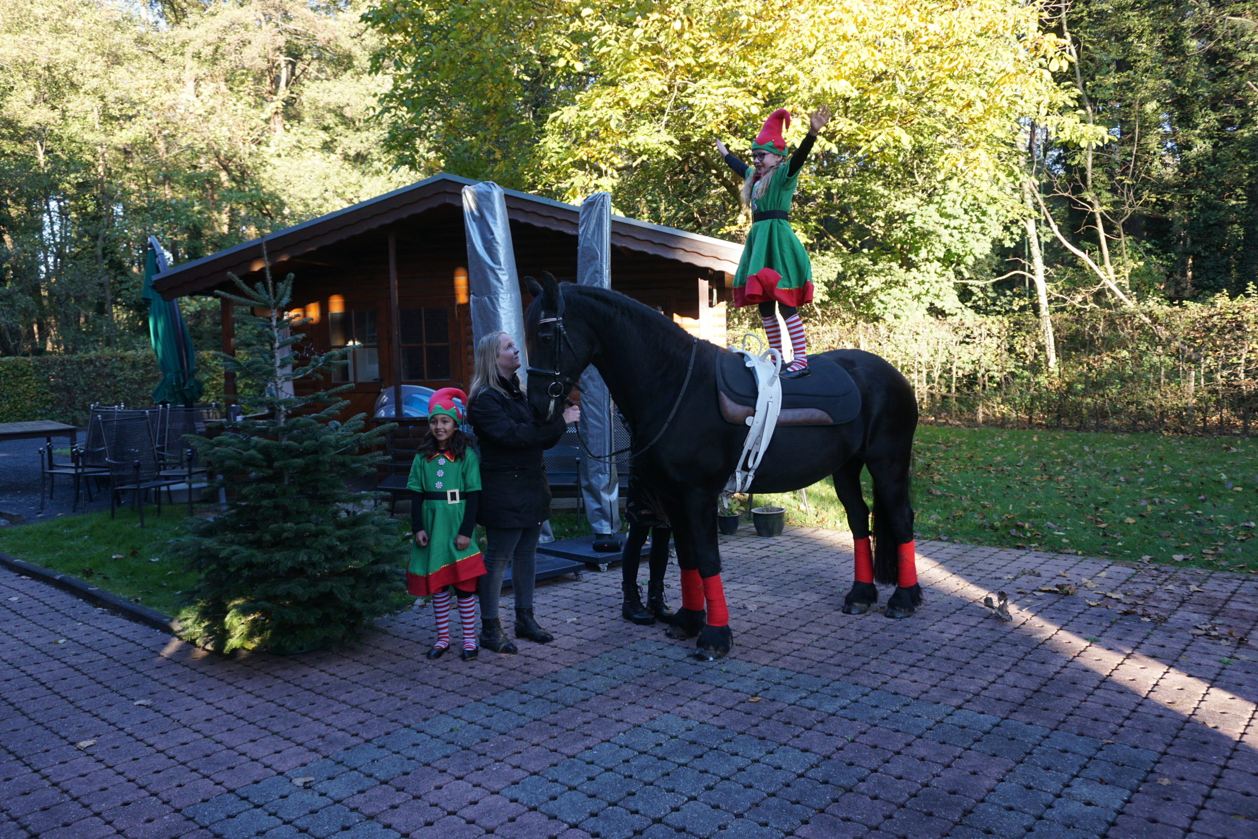 Ein Kind reitet ein schwarzes Pferd vor einem kleinen Häuschen. Es trägt grüne Kleidung mit roten Socken.