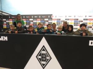 Gruppe von Kindern und Jugendlichen, die an einem Fußball-Event teilnehmen, stehen vor einer Bannertafel mit dem Logo von Borussia Mönchengladbach.