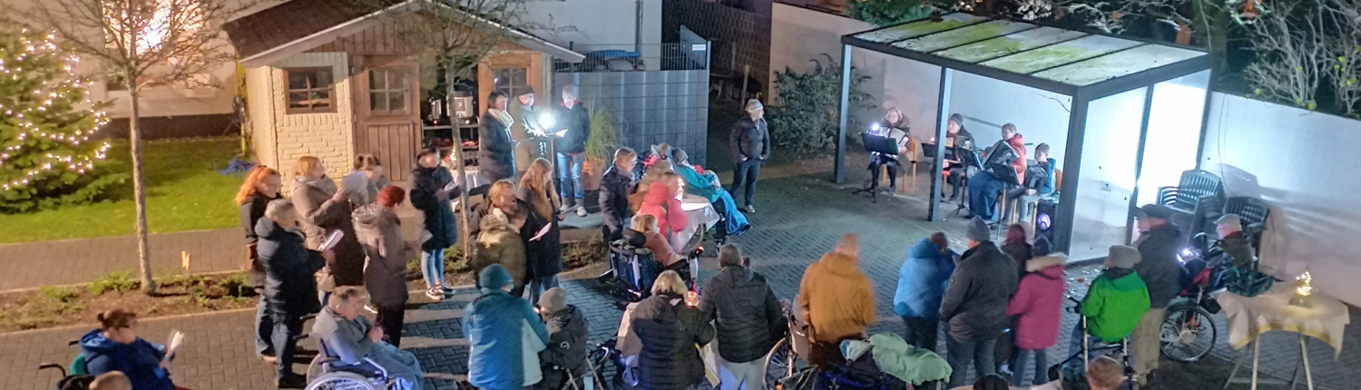 Viele Leute stehen draußen bei Nacht. Manche haben Kinder in Kinderwagen. Es ist hell erleuchtet.
