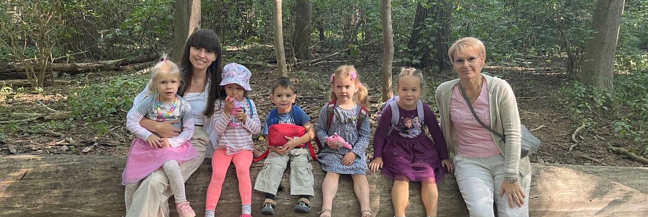 Eine Frau sitzt mit vier Kindern auf einem Baumstamm im Wald. Sie lächeln alle.
