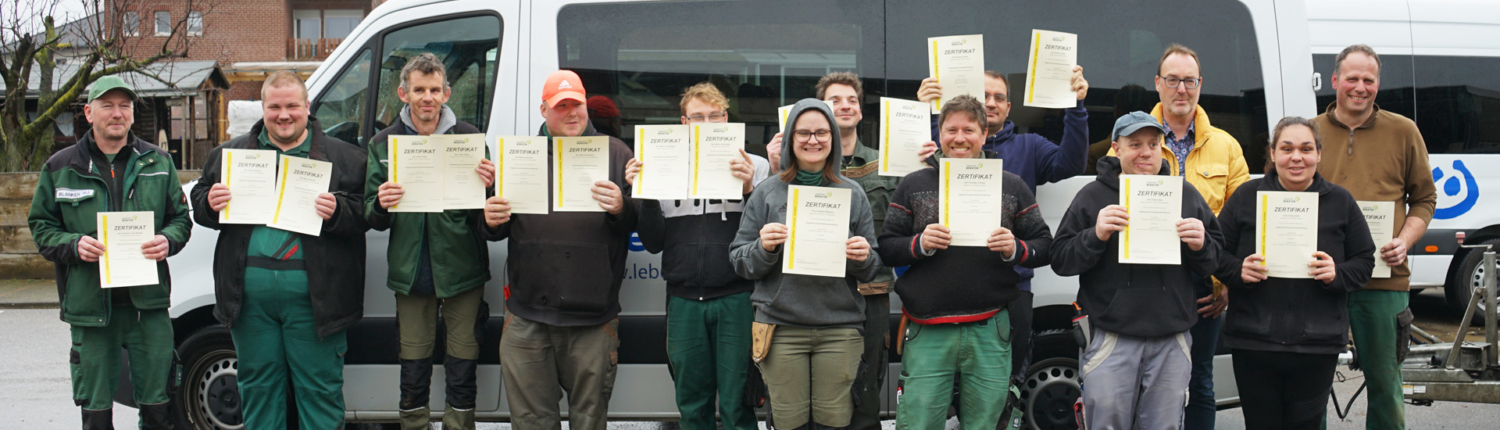 Gruppe von Teilnehmern mit Zertifikaten vor einem Transporter, die ihren erfolgreichen Abschluss einer Schulung oder Ausbildung feiern.