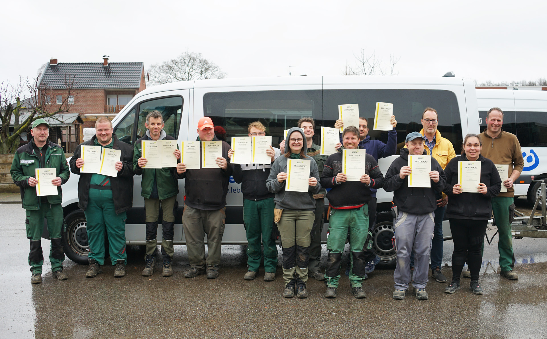 Gruppe von Teilnehmern mit Zertifikaten vor einem Transporter, die ihren erfolgreichen Abschluss einer Schulung oder Ausbildung feiern.