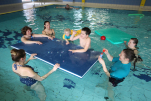 Familienaktivität im Schwimmbad mit Kindern, die auf einem Schwimmbrett spielen und Spaß im Wasser haben.