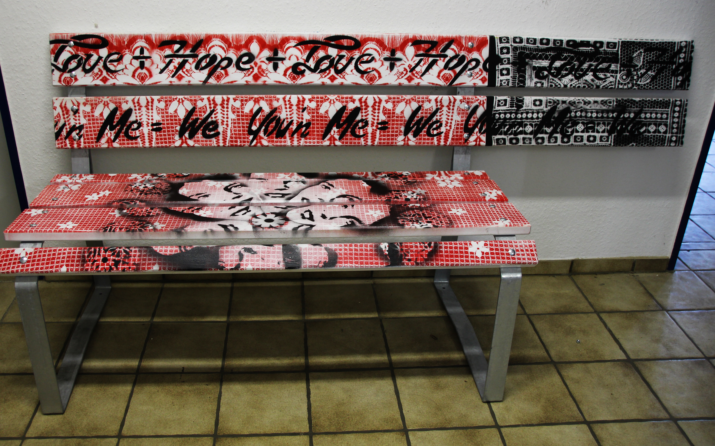 Bunte Graffiti-Bank mit roten und schwarzen Mustern, auf einem Fliesenboden platziert. Ideal für kreative Räume oder als Kunstinstallation.