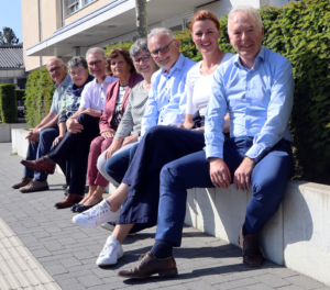 Fünf Personen sitzen auf einer Mauer. Sie lächeln und schauen in die Kamera.