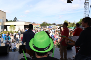 Eine Band spielt vor vielen Leuten draußen. Einige Leute schauen zu und machen Fotos.