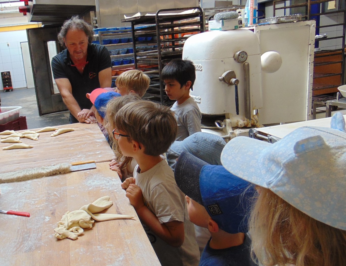 Kinder schauen einem Mann beim Brotbacken zu. Es gibt viel Mehl und Brot auf dem Tisch.