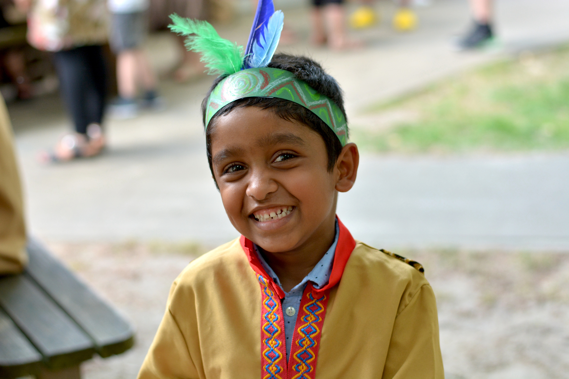 Lächelnder Junge in traditioneller Kleidung mit Federschmuck, spielt im Freien.