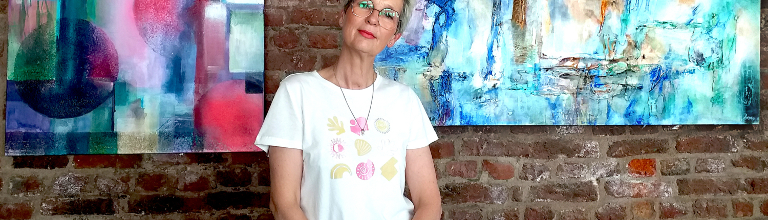 Eine Frau steht vor einem Bild. Das Bild hat bunte Farben und sieht aus wie ein Landschaftsbild. Die Frau trägt ein weißes T-Shirt.