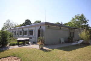 Moderne Gartenwohnung mit Terrasse und Rasenfläche, umgeben von Bäumen und strahlend blauem Himmel.